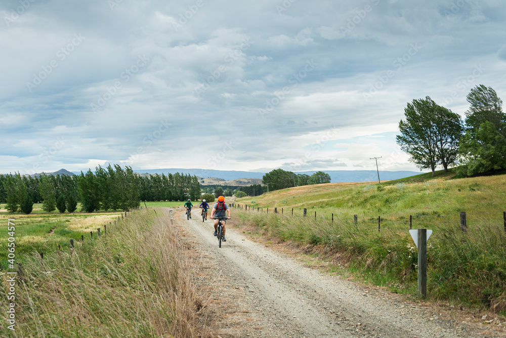 Three people cycling the Otago Central Rail Trail under the cloudy sky, South Island, New Zealand