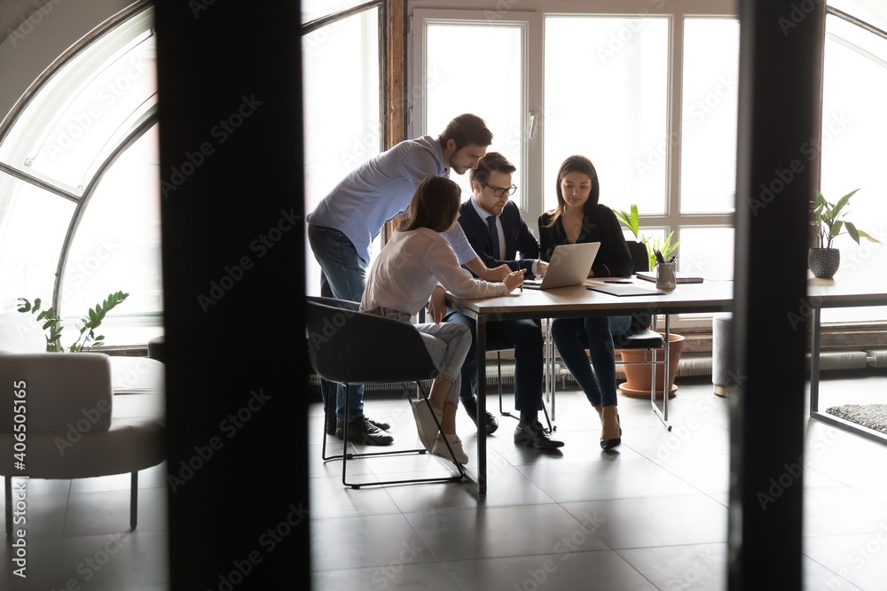Diverse employees team with leader wearing glasses working together in modern boardroom behind glass wall, colleagues looking at laptop screen, discussing project statistics, sharing ideas