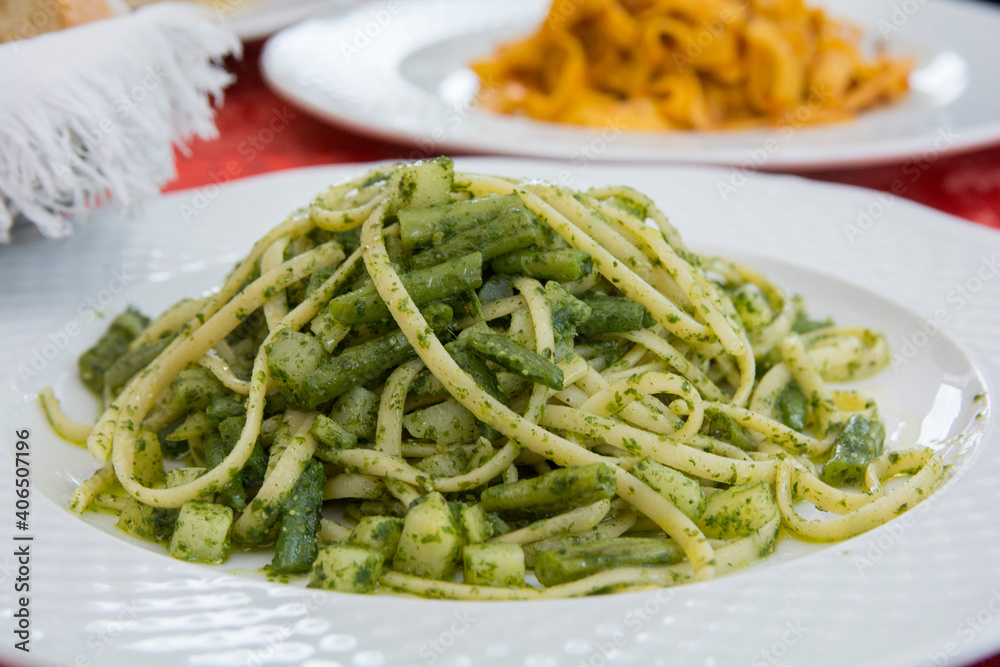 Close up view of a traditional green pasta dish: green Spaghetti with green bean and zucchini, served in a white plate