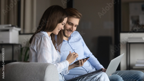 Happy colleagues using smartphone together, chatting, discussing news, spending break with gadgets, sitting on couch in modern office, smiling businessman and businesswoman working on project