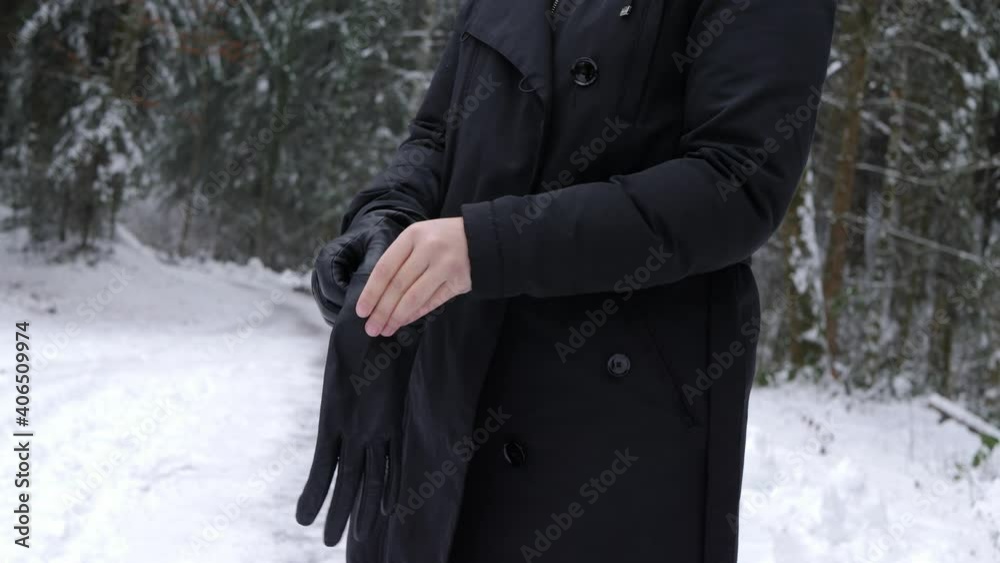 Young woman putting on leather gloves in the park with trees covered with snow. Young woman putting on leather gloves in the park with trees covered with snow.