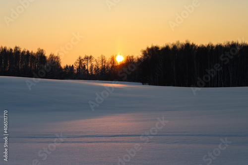 The path of the sun in the snow. Sunset in the snow. Cold winter evening at sunset. Frosted trees in the evening sun. Orange sky in the winter evening. Romantic sunset on a winter evening. Winter.