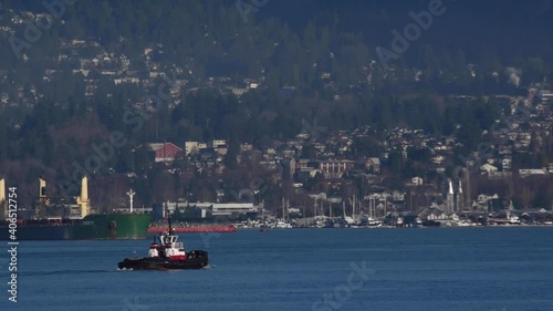 Tugboat sailing in Vancouver harbour for its next drag command with a green multi purpose vessel in the background. Wide steady shot photo