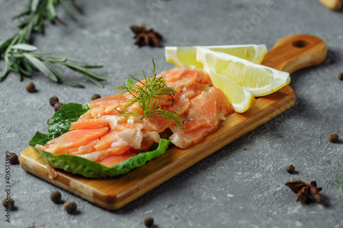 Pieces of fried salmon with dill and lemon wedges on a wooden board