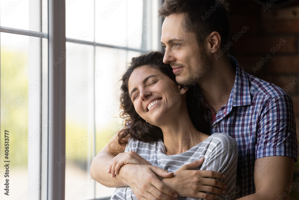 Close up of smiling young Caucasian man and woman hug embrace enjoy tender romantic moment at home together. Happy millennial couple renters cuddle look in distance dreaming imagining family future.