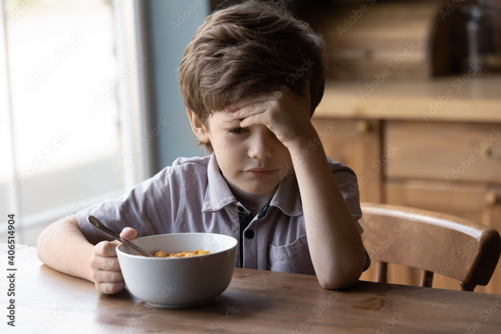 Unhappy little Caucasian boy child sit at table at home kitchen have no appetite for tasty healthy breakfast. Upset stressed small kid refuse to eat delicious organic cereals with milk. Diet concept. Unhappy little Caucasian boy child sit at table at home kitchen have no appetite for tasty healthy breakfast. Upset stressed small kid refuse to eat delicious organic cereals with milk. Diet concept.