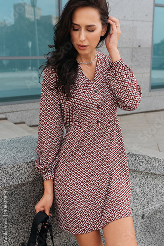 Young elegant girl posing at city street. Pretty beautiful business woman in elegant dress against city background.