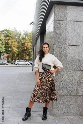 Young elegant girl posing at city street. Pretty beautiful business woman in elegant dress against city background.