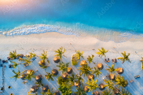 Fotografia Aerial view of umbrellas, green palms on the sandy beach at sunset