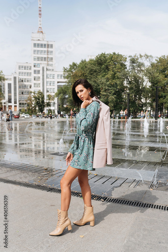 Young elegant girl posing at city street. Pretty beautiful business woman in elegant dress against city background.