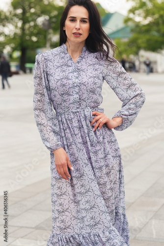 Young elegant girl posing at city street. Pretty beautiful business woman in elegant dress against city background.
