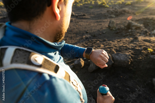 Man doing senderism, while looking at his smartwach in the sunset photo