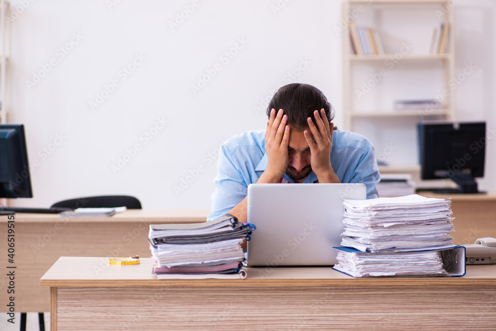 Young male employee unhappy with excessive work in the office Young male employee unhappy with excessive work in the office