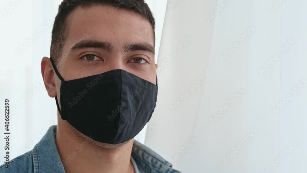 Hispanic man in casual shirt standing indoors wearing a protective black mask on his face and looking directly into the camera. Healthcare concept Hispanic man in casual shirt standing indoors wearing a protective black mask on his face and looking directly into the camera. Healthcare concept