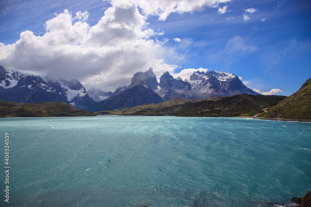 Torres del Paine vista surrounded by white fluffy clouds and blue sky. 
