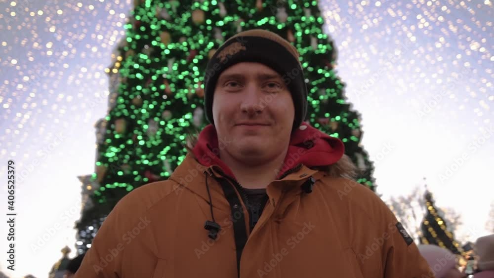 Portrait of a young cheerful man smiling and a Christmas tree, bokeh of lights of a Christmas garland in the background. Guy in a hat and a yellow jacket Portrait of a young cheerful man smiling and a Christmas tree, bokeh of lights of a Christmas garland in the background. Guy in a hat and a yellow jacket