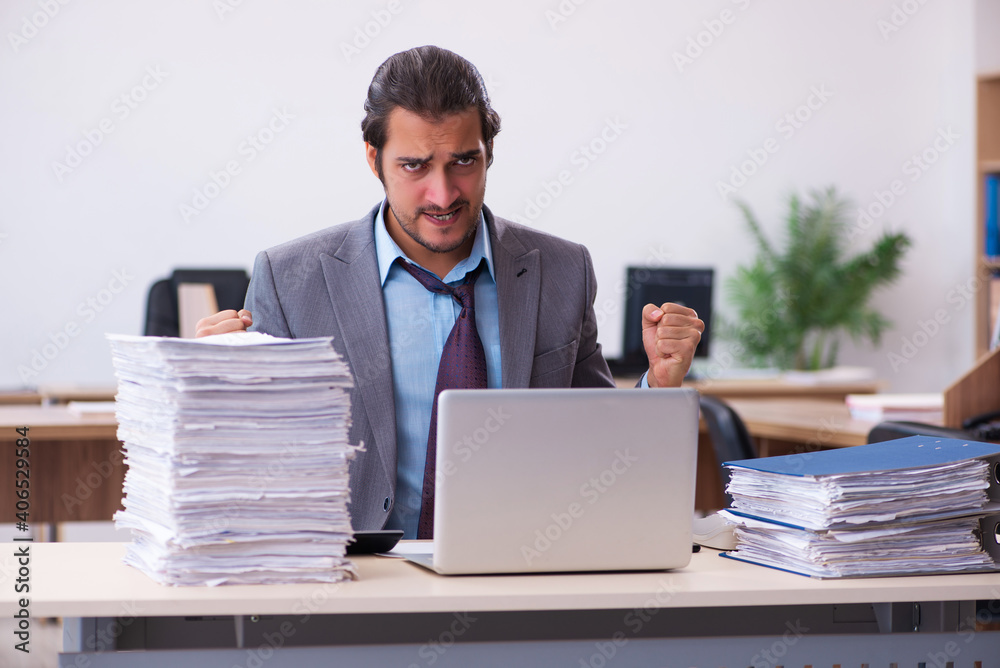 Young male employee unhappy with excessive work in the office Young male employee unhappy with excessive work in the office