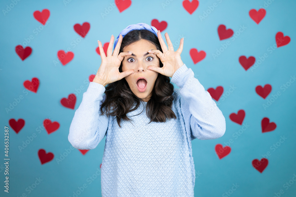 Young beautiful woman over blue background with red hearts Trying to open eyes with fingers, sleepy and tired for morning fatigue