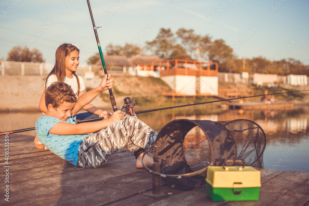 Two young happy little friends, boy and girl fishing on a lake in a sunny summer day Two young happy little friends, boy and girl fishing on a lake in a sunny summer day