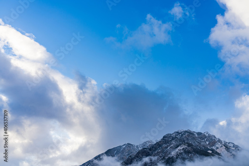 Snowy mountain peak surrounded by clouds in a sunny day morning with blue sky.
