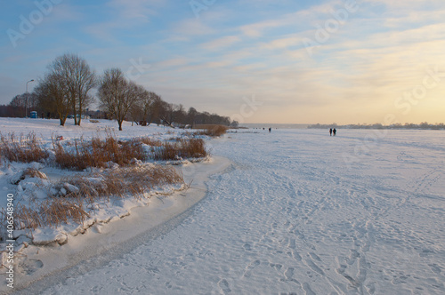 winter landscape. frozen river in winter on the background of the blue sky during sunset, people walk admiring the beautiful nature © fotofotofoto