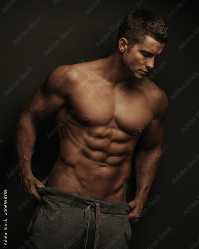 Male fitness model standing on black background with holding his pants
