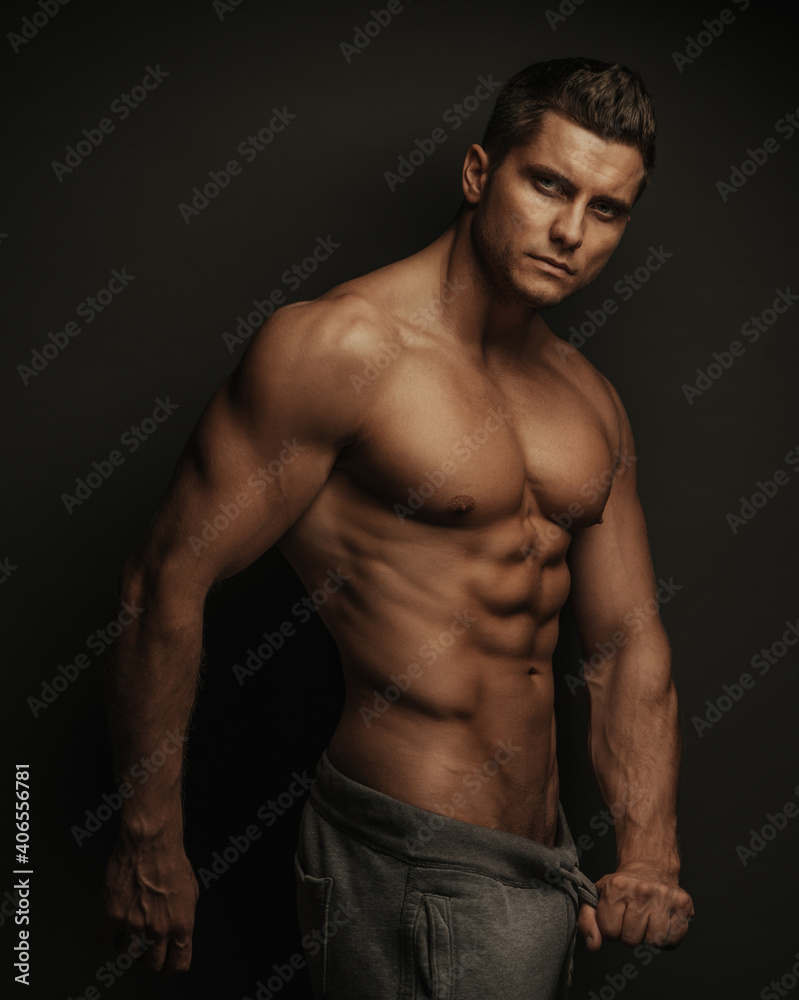 Male fitness model standing on black background with holding his pant's ropes Male fitness model standing on black background with holding his pant's ropes