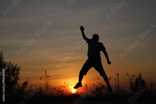 The cheerful young man jumped high and stepped on the sun in the silhouette.