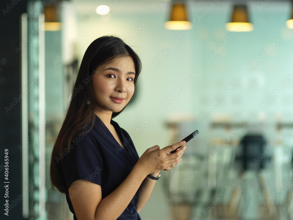 Businesswoman smiling to camera while using smartphone in office room Businesswoman smiling to camera while using smartphone in office room