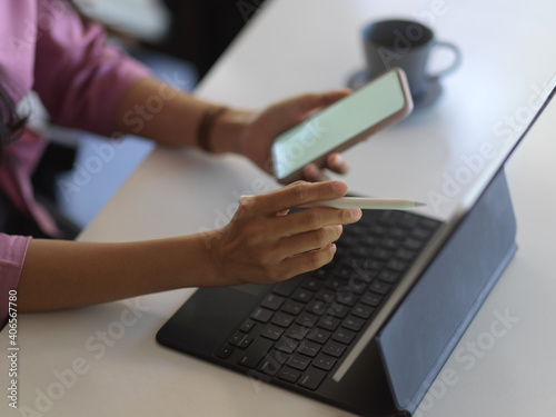 Female hands working smartphone and digital tablet on the table in office room