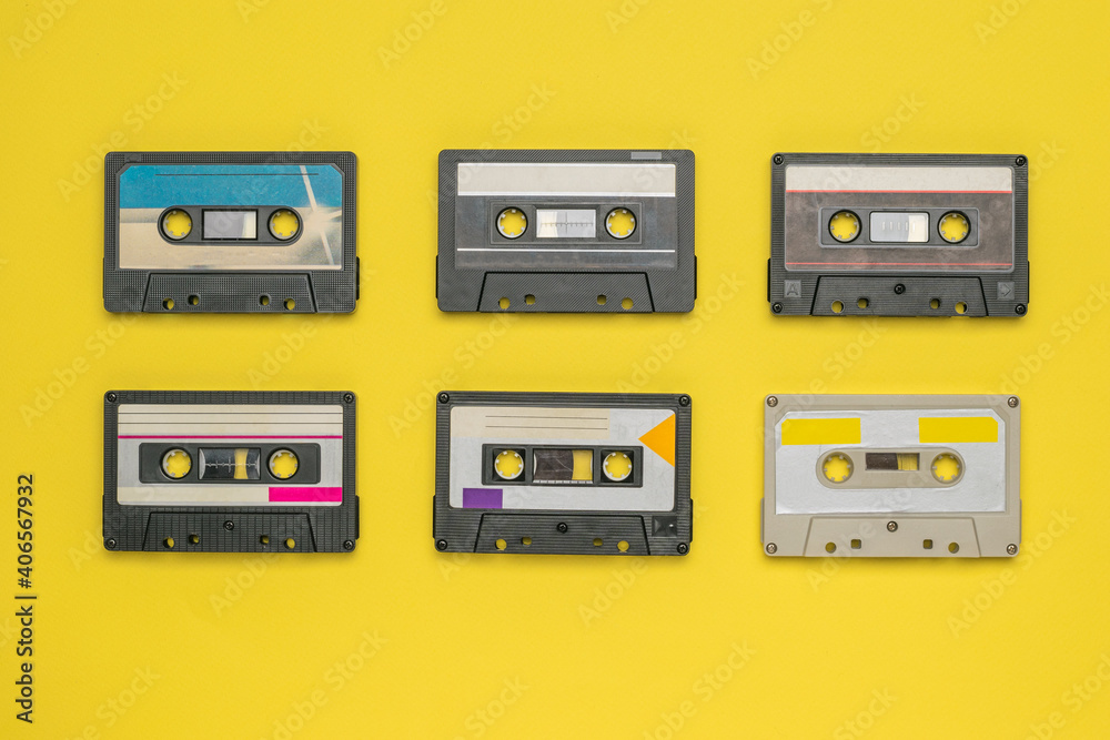 Six audio cassettes with magnetic tape on a yellow background.