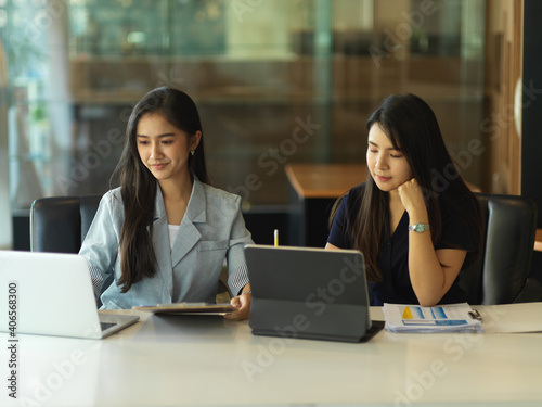 Two businesswoman working with laptop while sitting in meeting room