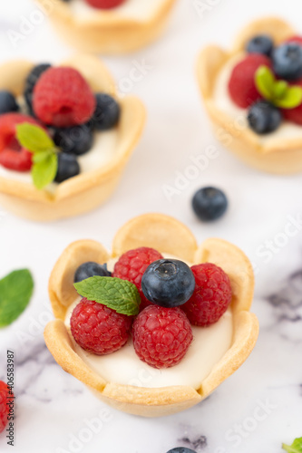 Delicious pastry mini fruit cream cheese pies or tart cakes with fresh raspberry, blueberry and blackberry