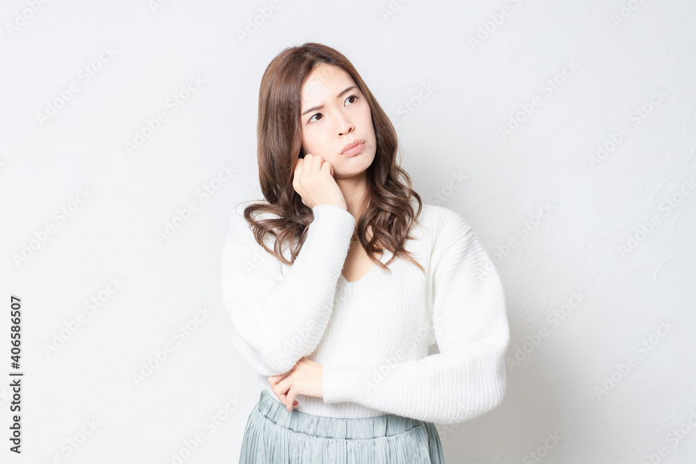白い壁の前に立って考え事をする若い女性 白い壁の前に立って考え事をする若い女性