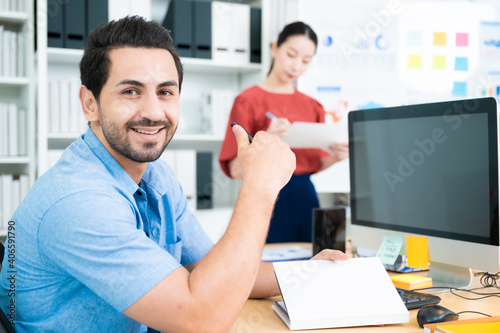 Young asian man working on a computer at workplace. He looked straight at the camera and smile
