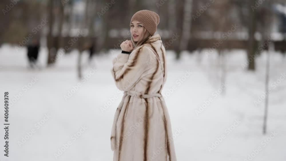 An attractive fashionable blonde in a beautiful fur coat and a beige hat poses against the background of a winter park. Model on a snowy background of winter weather. An attractive fashionable blonde in a beautiful fur coat and a beige hat poses against the background of a winter park. Model on a snowy background of winter weather.