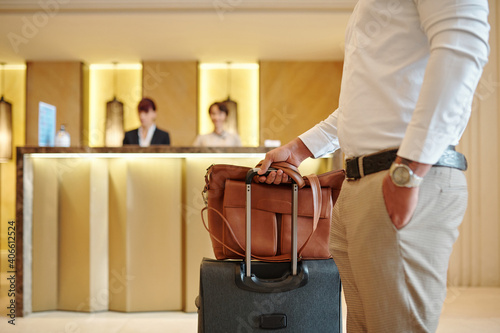 Cropped image of hotel guest standing in lobby with luggage after checking in