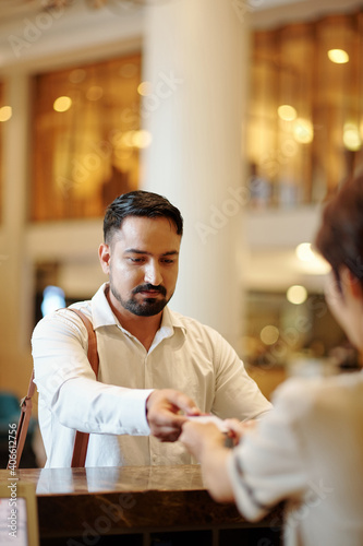 Bearded serious man returning electronic room key to manager at hotel reception
