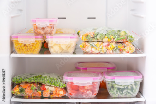 Containers and plastic bags with frozen vegetables in refrigerator