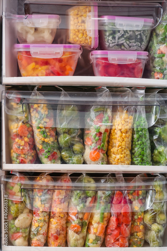Containers and plastic bags with frozen vegetables in refrigerator, closeup