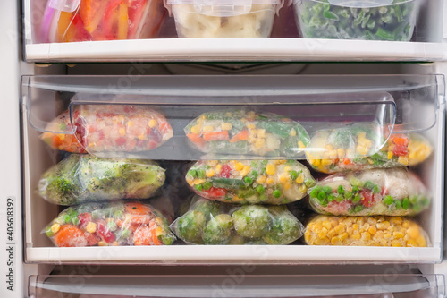 Plastic bags and containers with frozen vegetables in refrigerator