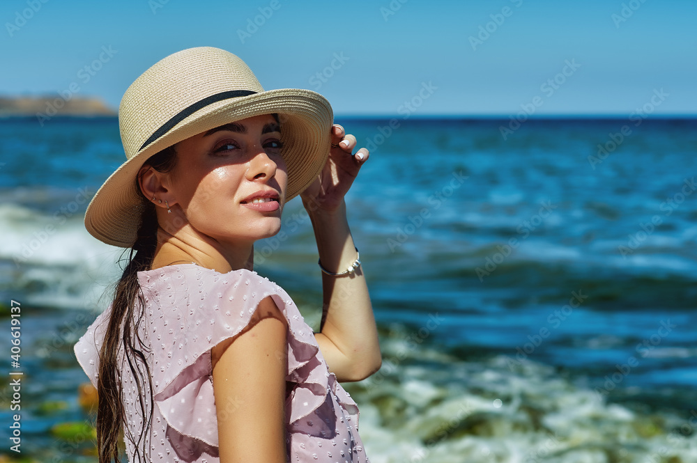 Portrait of a young beautiful woman in a straw hat on a walk by the sea
