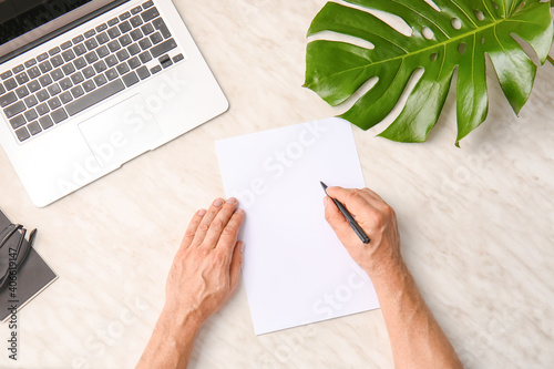 Male hands with blank paper sheet and laptop on light background