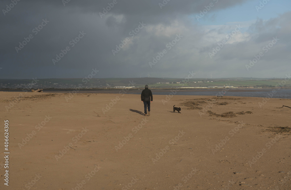 Adult Male and a Black Schnoodle Dog Walking on the Beach at Crow Point by Braunton Burrows on the North Coast in Devon, England, UK
