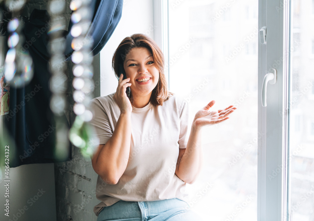 Beautiful happy sensual brunette young woman plus size body positive speaking by mobile phone at the home Beautiful happy sensual brunette young woman plus size body positive speaking by mobile phone at the home