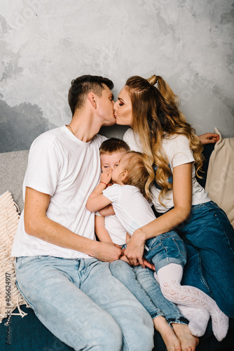 Family portrait of parents and children in denim casual style clothes. Fashion models kissing on gray background. Smiling young mother and father with daughter and son posing together.