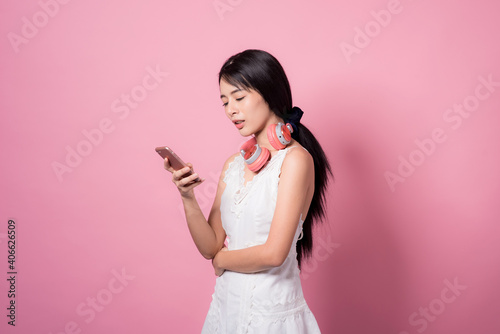 Happy smiling young asia woman with headphones enjoying listens to music over pink background