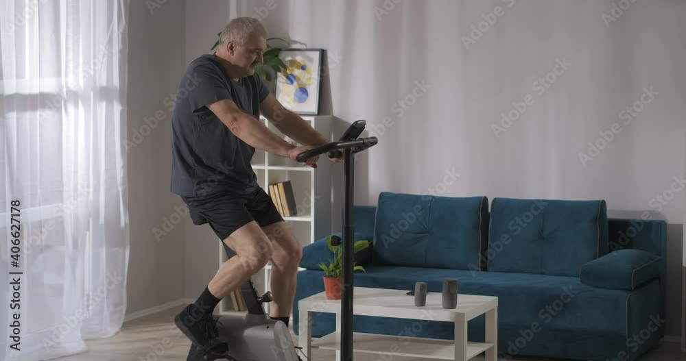 keeping fit and good physical condition by workout on stationary bike, middle aged man is training alone at home keeping fit and good physical condition by workout on stationary bike, middle aged man is training alone at home