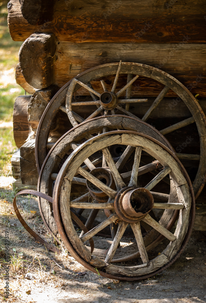 Wooden wheels from an ancient cart standing in front of the wall of a wooden country cottage