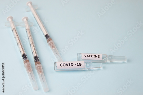 Two ampoules of the Covind-19 vaccine and three syringes on a light blue background